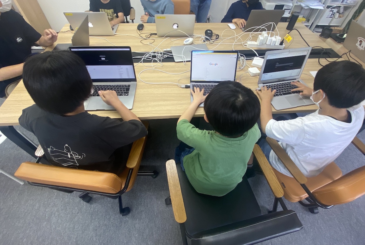 テーブルを囲んでノートパソコンで作業する生徒たち